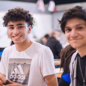 Two young males smiling and posing for the photo in an indoor setting during a transition iep goals bank meeting, possibly at a school or a casual gathering.