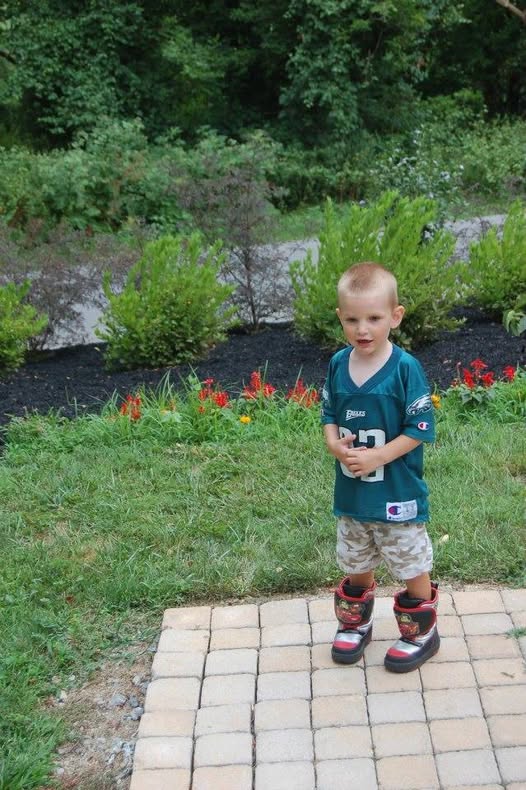 Young boy trying on new shoes outdoors on a brick patio.
