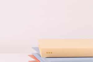Close-up of a stack of closed books with pastel-colored covers, including beige, blue, and red, resembling the vibrant assortment you might find when you're ready to get school records against a plain white background.