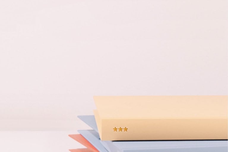 Close-up of a stack of closed books with pastel-colored covers, including beige, blue, and red, resembling the vibrant assortment you might find when you're ready to get school records against a plain white background.