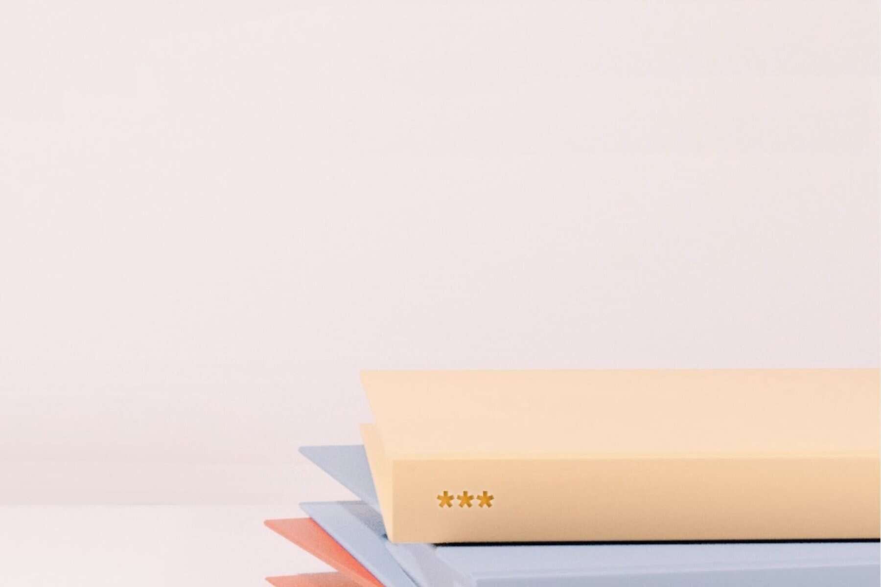 Close-up of a stack of closed books with pastel-colored covers, including beige, blue, and red, resembling the vibrant assortment you might find when you're ready to get school records against a plain white background.