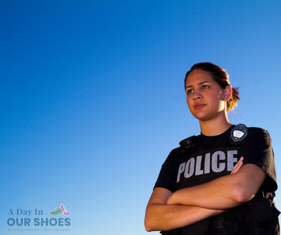 A police officer, embodying community support, stands with arms crossed against a clear blue sky. Clad in a black shirt emblazoned with "police" and a utility vest, he represents the teamwork akin to iep parent participation. The logo text "a day in our shoes" rests at the bottom left.
