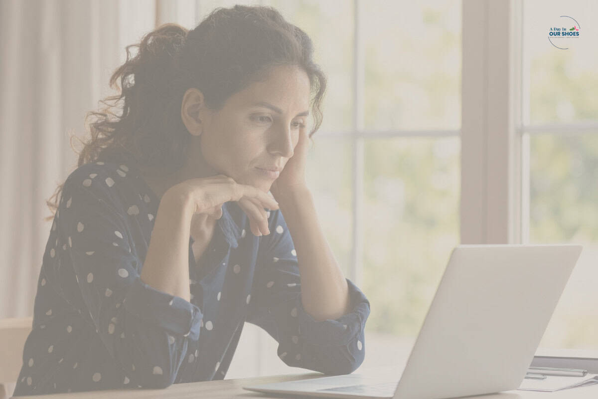 A person with dark curly hair wearing a polka-dot shirt sits at a table, looking intently at a laptop screen in a bright room, researching what can you ask for on iep.