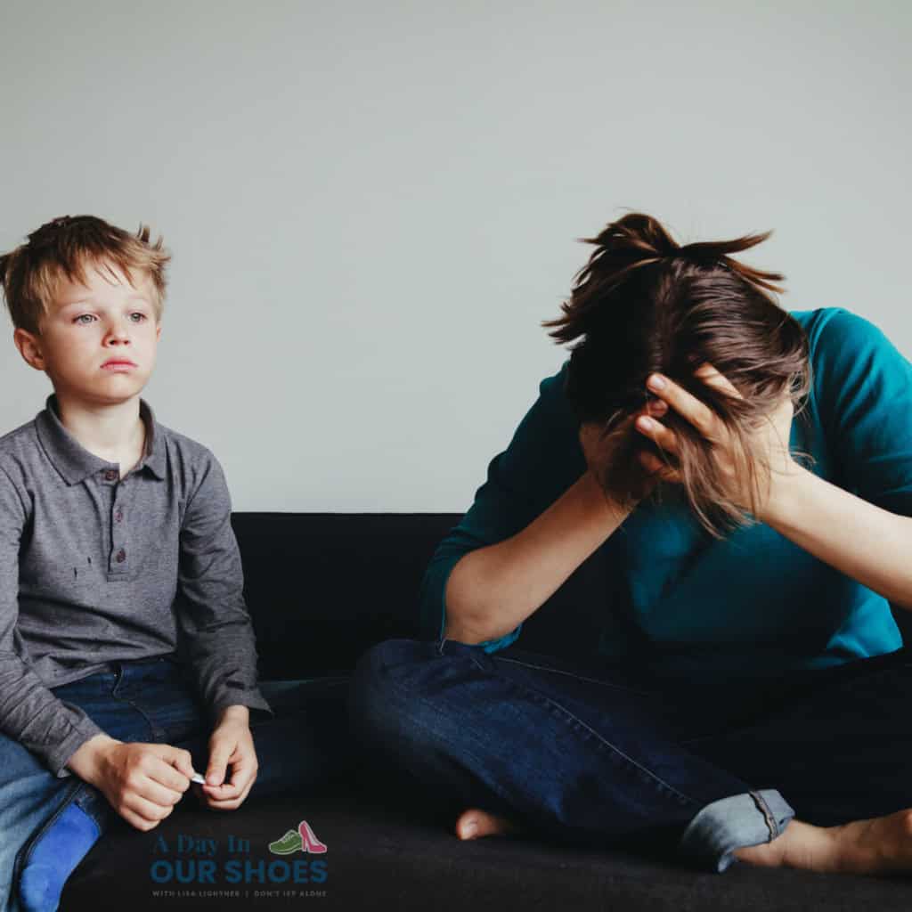 A young boy, recently suspended from school, sits on a couch next to an adult who is sitting with their head in their hands, appearing distressed.