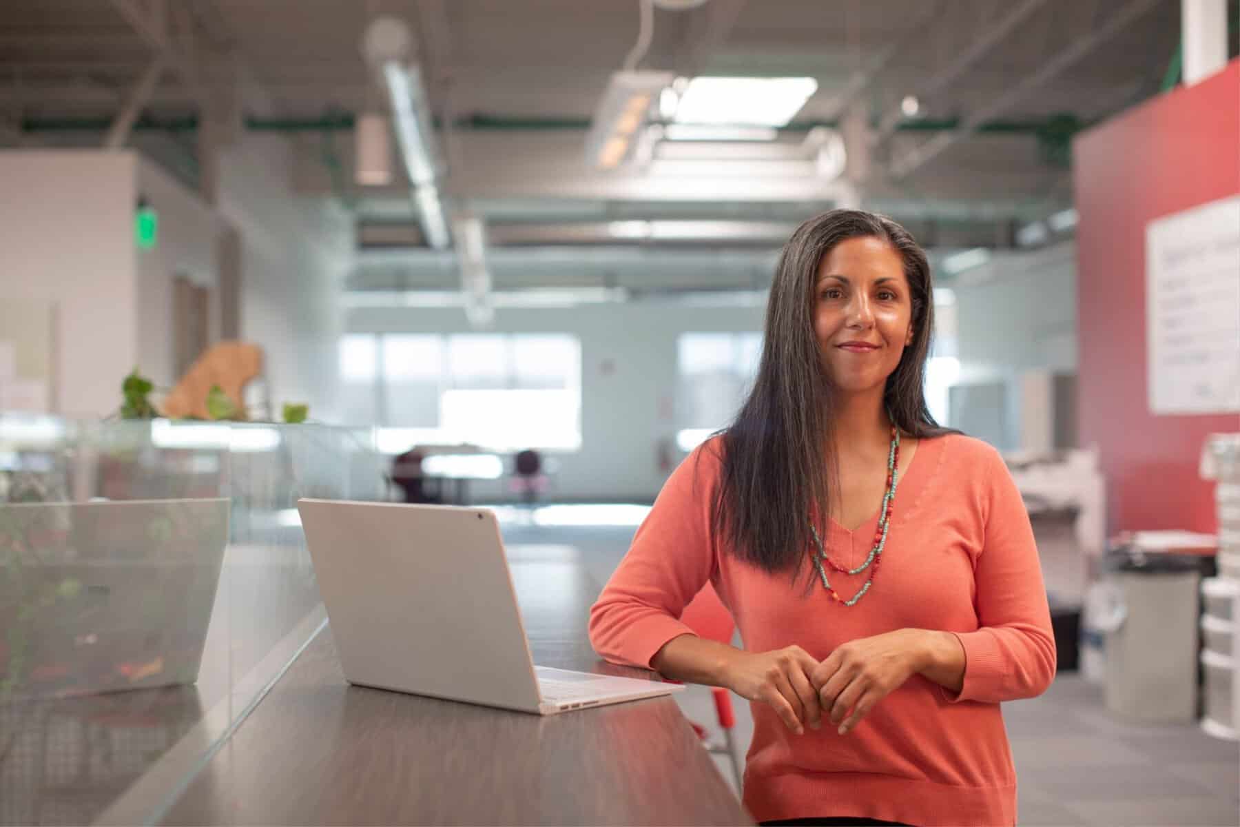A woman standing in front of a desk with a laptop, working as an iep advocate.