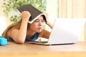 A girl using a laptop to work and complete tasks, while holding her head up.