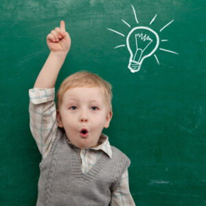 A young boy standing in front of a chalkboard with a light bulb drawn on it, learning techniques to improve slow processing speed in kids.