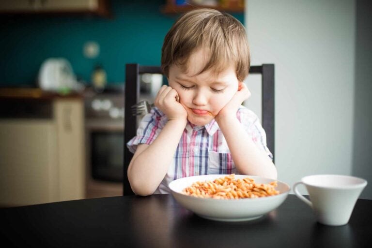 A young boy sitting at a table with a bowl of cereal, focused on his meal.