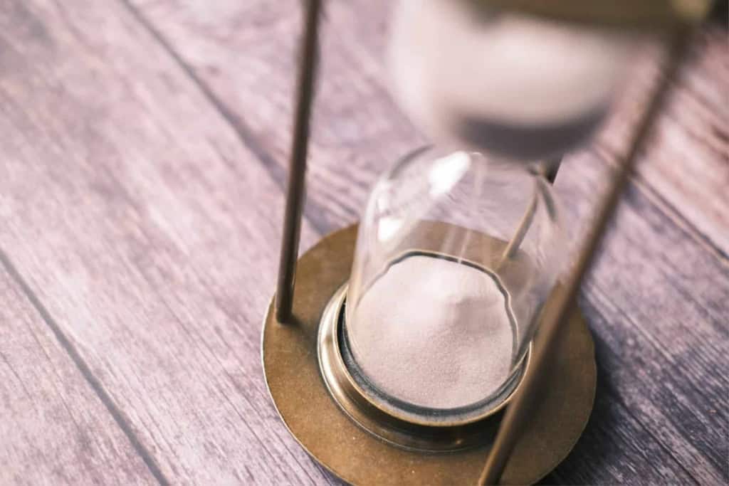 Close-up of a sand timer on a wooden surface for time management.