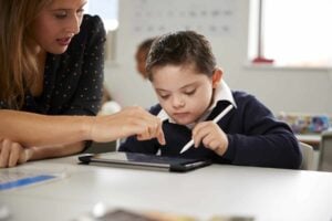 Boy working with his teacher while using an aac communication device in a classroom setting