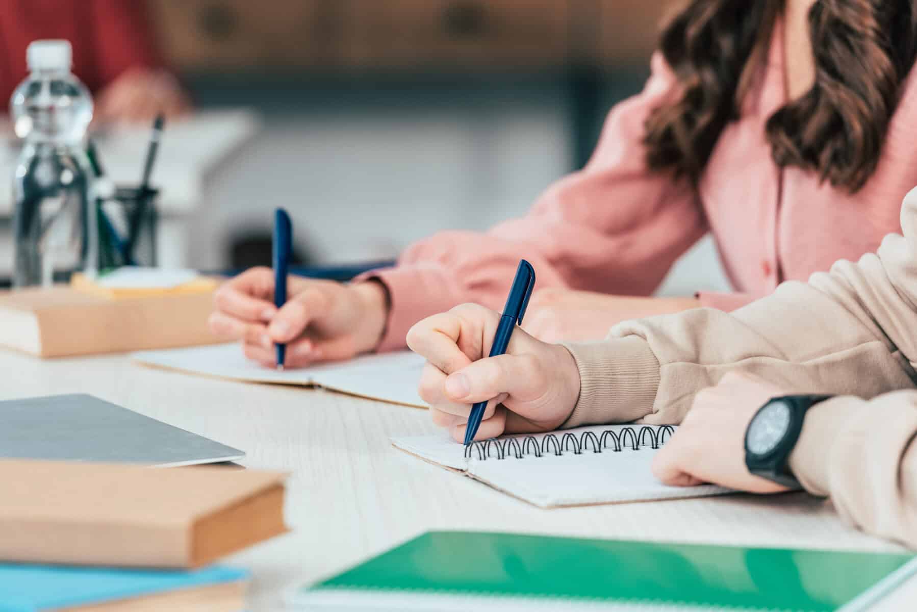 Two people sit at a table, pens in hand, thoughtfully jotting down notes on executive functioning strategies in their notebooks.