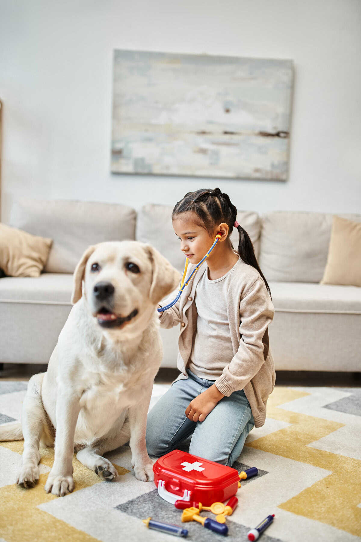 A little girl is engaging in pretend play with a dog, using a stethoscope to mimic a doctor's examination.