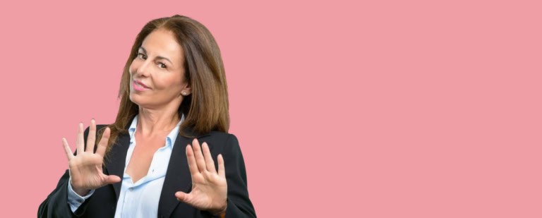 A woman in a business suit making a "stop" gesture with her hands against a pink background.