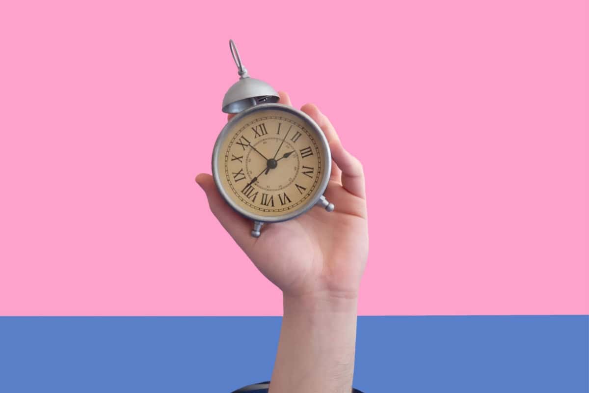25 measurable telling time iep goals 1 A hand is holding an analog alarm clock against a split pink and blue background, demonstrating telling time iep goals.