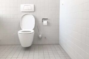 A clean and unoccupied bathroom with an open white toilet following toilet protocol for iep, toilet paper roll mounted on the wall, and tiled flooring.
