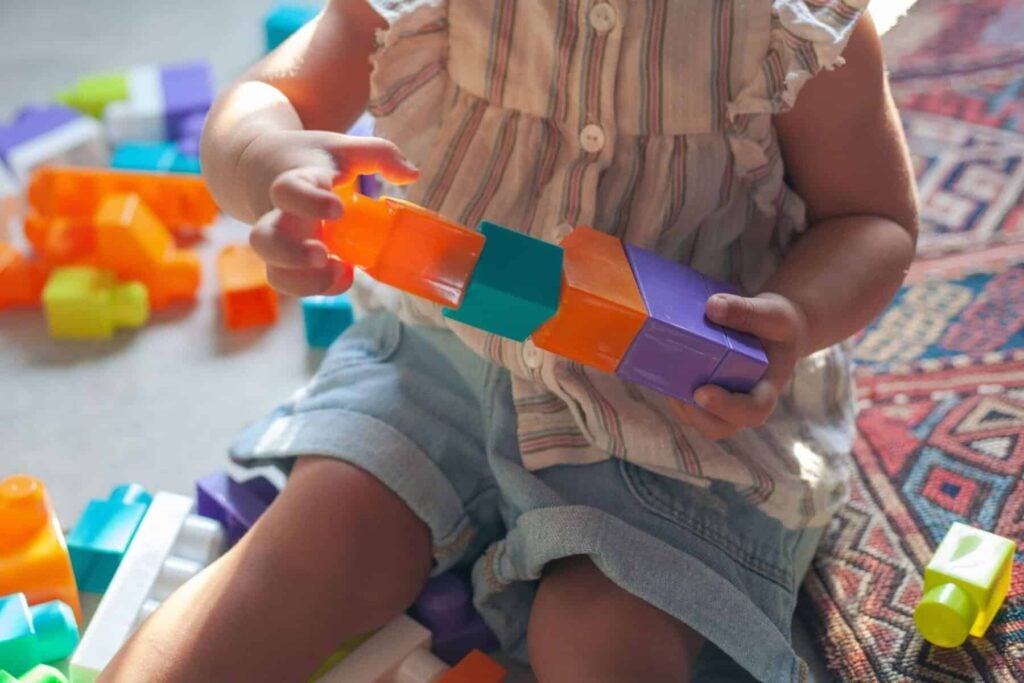 A child sitting and playing with colorful interlocking plastic blocks, experiencing the difference floortime approach makes in engagement.