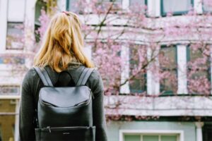 A person with blonde hair wearing a backpack stands facing a blooming cherry blossom tree, with measurable postsecondary goals for an iep outlined on the building in the background.