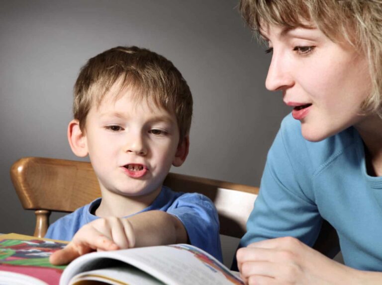 A young boy and a woman reading a book together, the boy is pointing at the page while the woman looks on attentively as part of his speech-only iep activities.