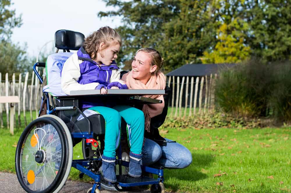 15 iep goals for severe and profound students: supporting students with high needs 1 A young girl in a wheelchair and a woman kneeling beside her, supporting students, share a moment, smiling at each other outdoors.