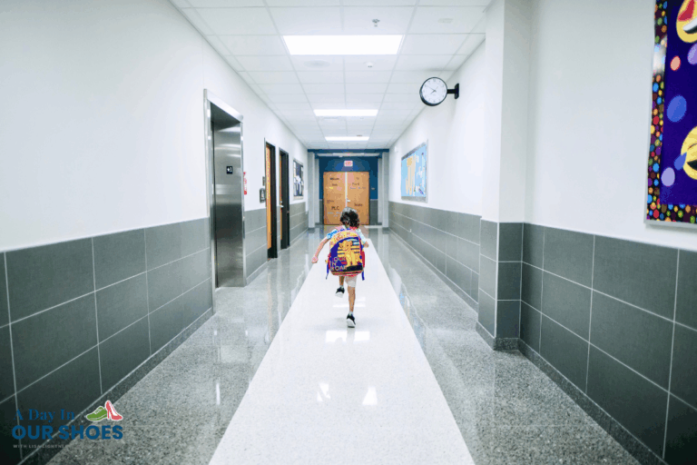 A young child with a colorful backpack, who is at risk of autism elopement, walks down a bright, empty school hallway with classrooms on either side and a clock on the wall.