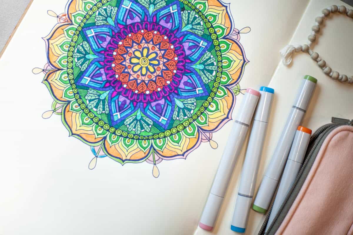 A vibrant mandala drawing graces the paper, crafted with four markers. Nearby, the partial view of a pink pencil case adds charm. Dive into creativity with our free mandala coloring pages for endless inspiration.