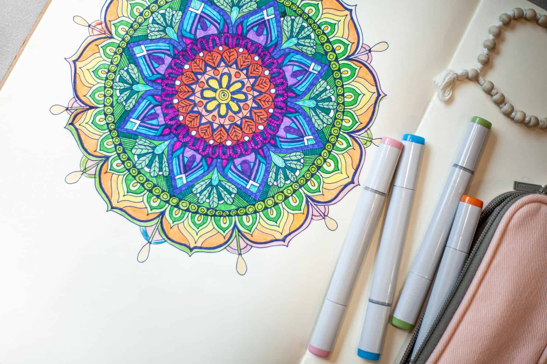 A vibrant mandala drawing graces the paper, crafted with four markers. Nearby, the partial view of a pink pencil case adds charm. Dive into creativity with our free mandala coloring pages for endless inspiration.