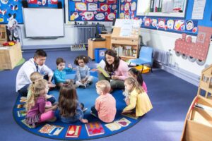 A teacher skillfully explores how to add more to circle time as she reads to a group of children seated in a circle on a colorful rug, surrounded by vibrant classroom artwork.