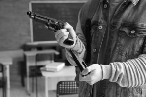 A person in a jacket is meticulously loading a handgun, simulating the process as part of school shooter drills in a classroom setting.