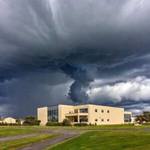 A dark, swirling storm cloud looms over a beige building surrounded by grass.