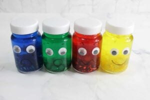 Four glitter sensory bottles filled with colorful liquid and vibrant glitter each sport googly eyes and unique drawn expressions: blue (sad), green (neutral), red (angry), and yellow (happy).