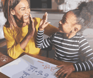 A woman and child sit at a table, smiling and high-fiving over math problems.