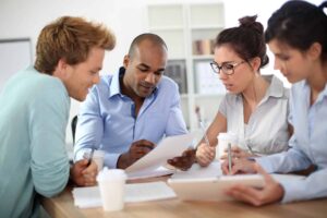 A multidisciplinary team of four people sits at a table, discussing papers and notes related to special education, with coffee cups nearby.