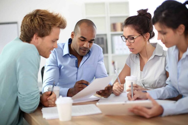A multidisciplinary team of four people sits at a table, discussing papers and notes related to special education, with coffee cups nearby.