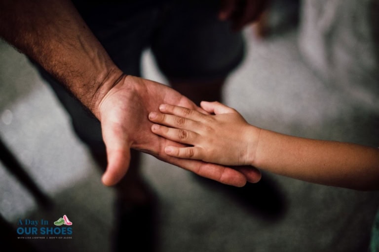 An adult hand and a child's hand touch palm to palm against a neutral background, symbolizing connection in education. The lower left corner features the logo "a day in our shoes.