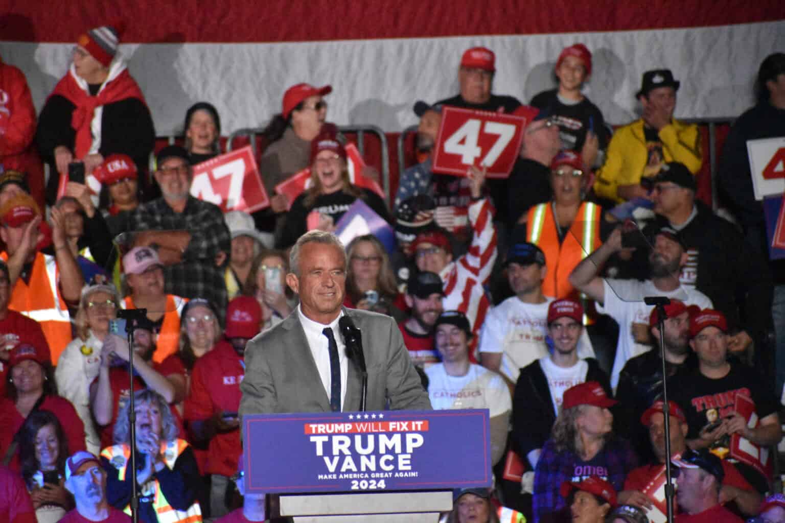 A man speaks passionately at a podium bearing signs for trump and vance 2024, with an energized crowd wearing red hats and holding "47" signs. The moment highlights the community strength reminiscent of values championed by the administration for community living (acl).