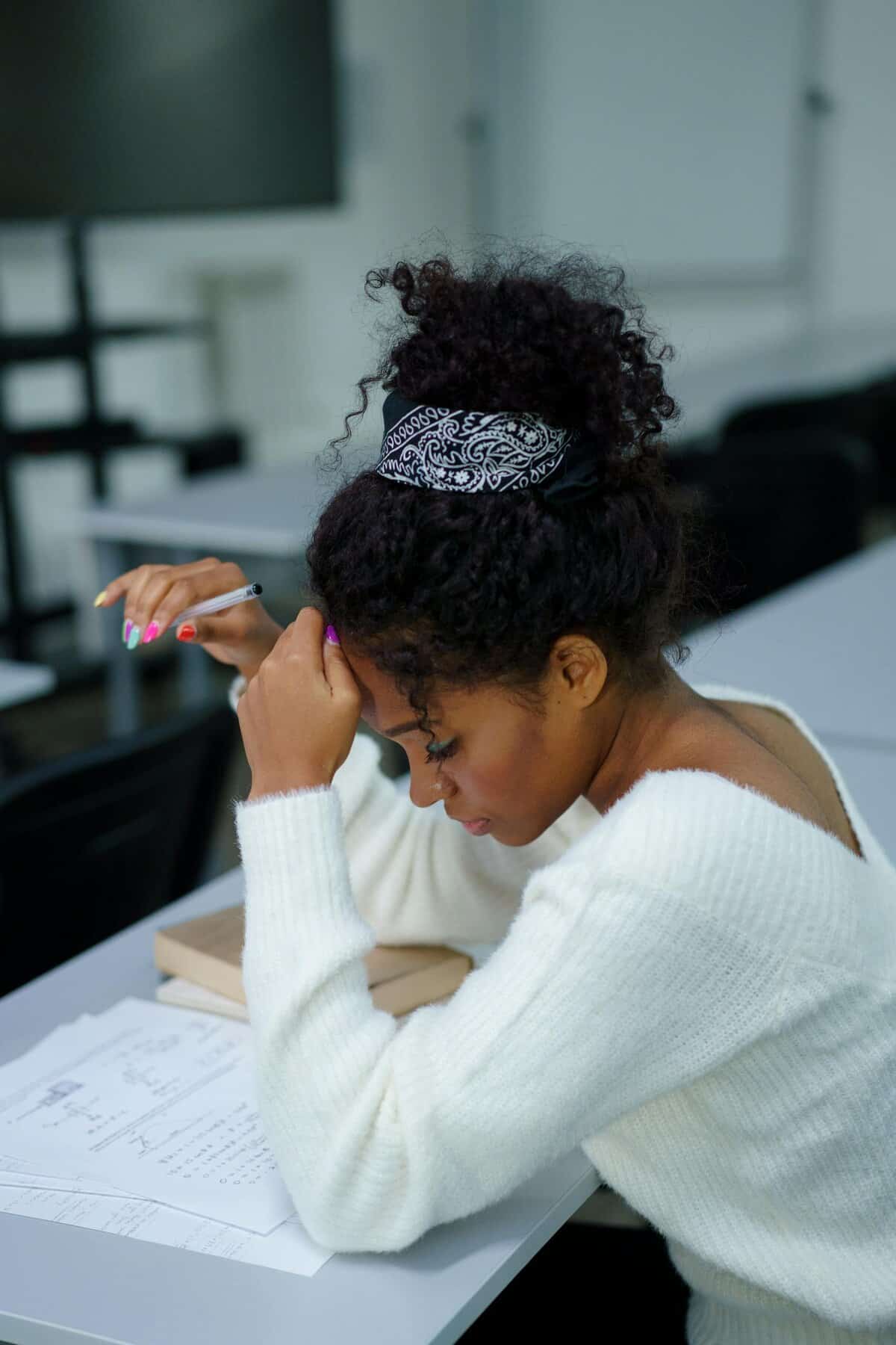 A young woman deeply concentrating while sitting at a desk with study materials.