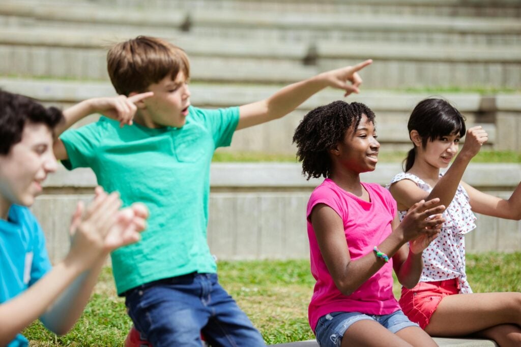 Group of diverse children cheering and clapping outdoors on a sunny day.
