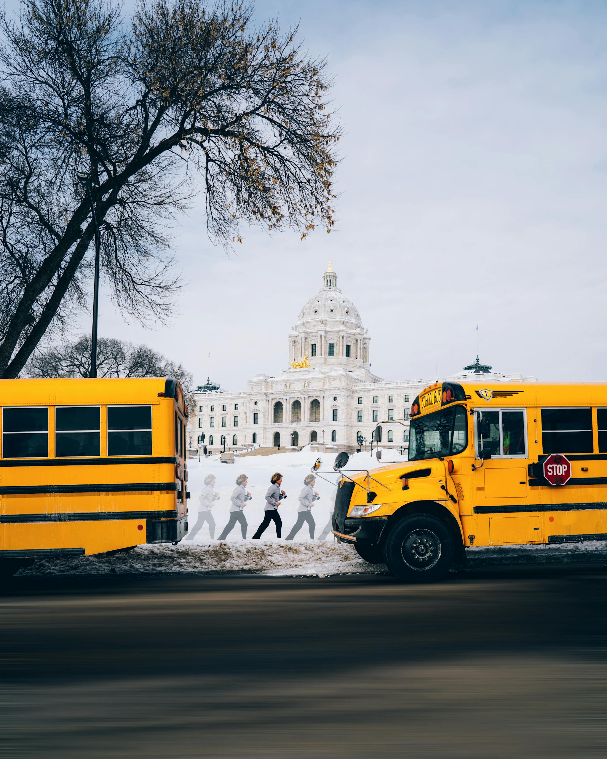 Yellow school buses parked in front of a snowy capitol building with pedestrians visible.