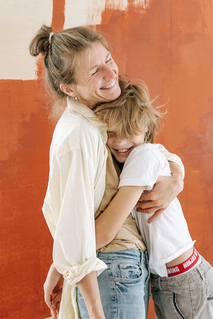 A heartwarming embrace between a smiling mother and son in front of a colorful painted wall.