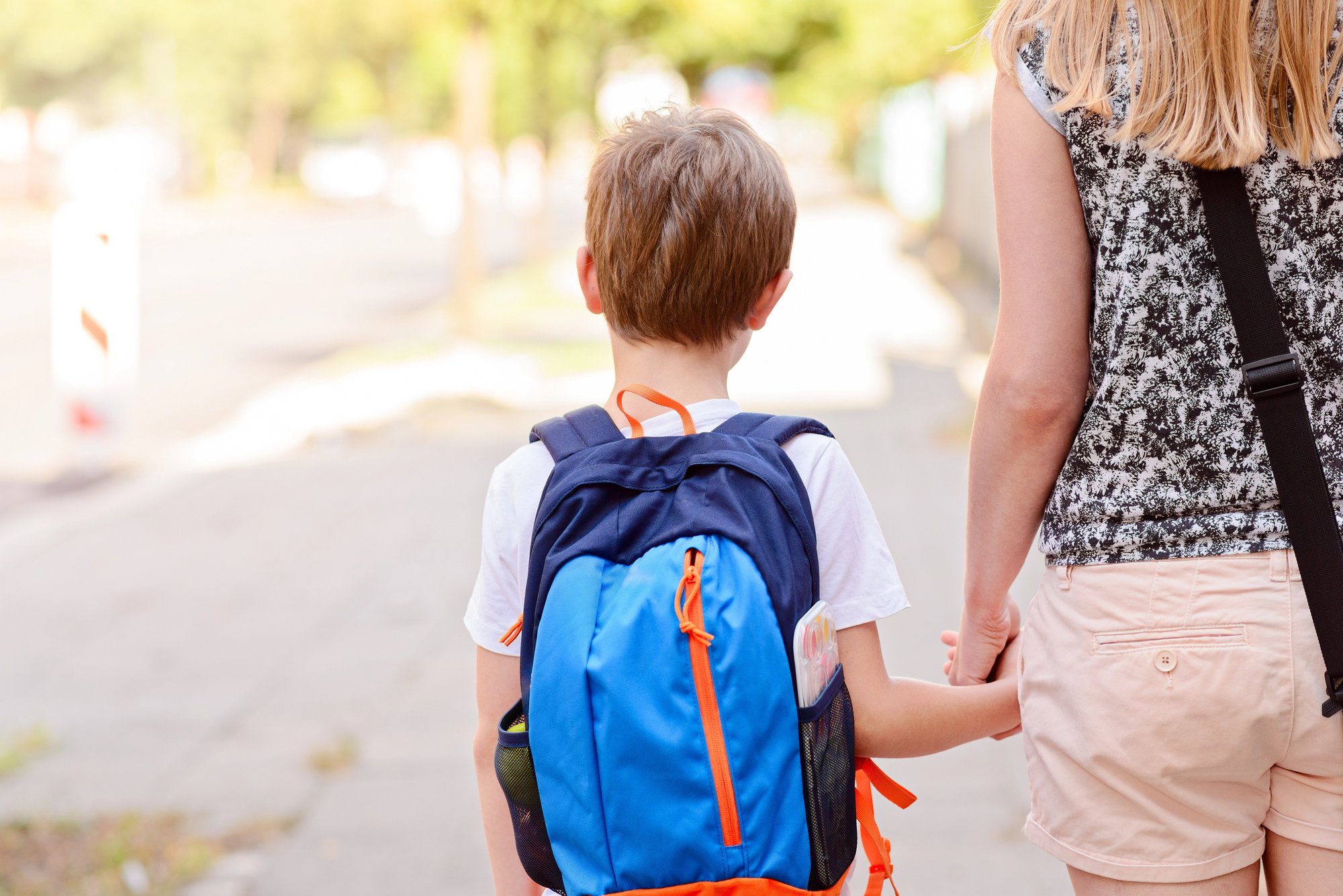 A young child with a blue backpack holds an adult’s hand while walking on a sidewalk in daylight, ready for school preparation with the support of iep parents.