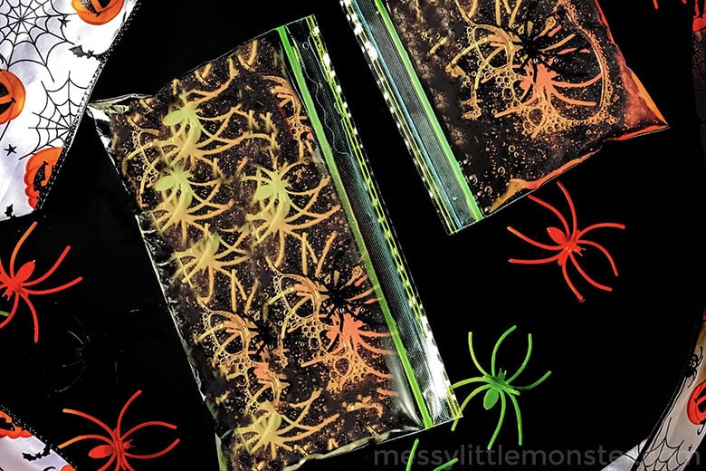 Two clear plastic bags filled with black liquid and plastic spider toys sit on a halloween-themed background, making them perfect for halloween sensory play or other non-food ideas for festive halloween activities.
