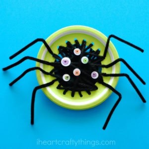 A spider craft made from black pipe cleaners, multiple googly eyes, and a yellow plastic lid, displayed on a blue background—perfect for halloween fine motor activities.