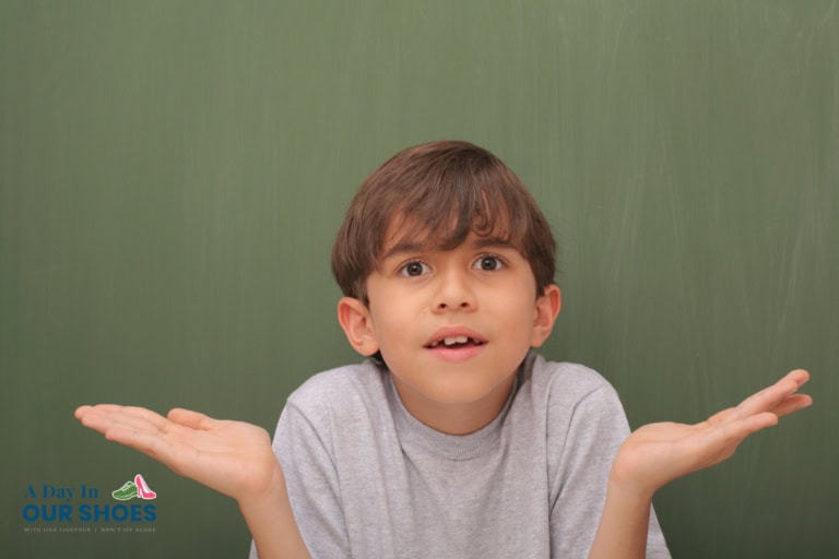Young boy with brown hair in a gray shirt stands in front of a chalkboard, raising both hands with a confused or questioning expression, highlighting challenges in communication. Logo in lower left corner reads "a day in our shoes.