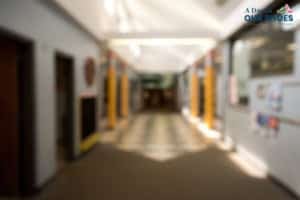 A blurry image of a school hallway with lockers and classroom doors on both sides under a bright ceiling light, hinting at the question: what is alternative schooling?.
