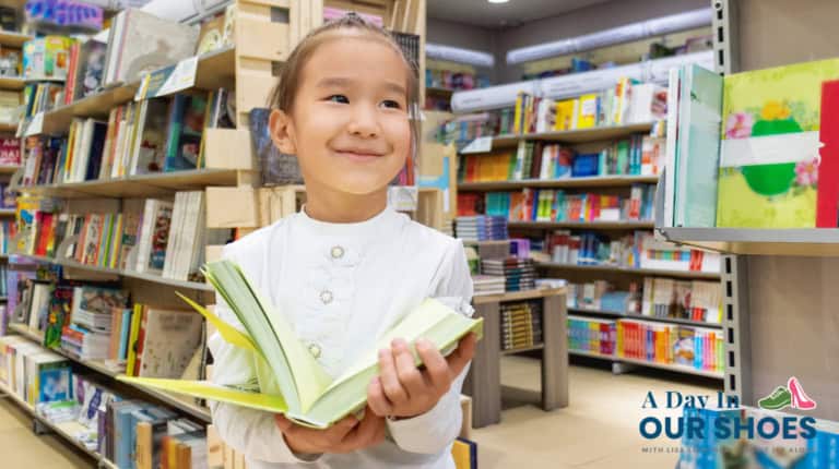 A young girl stands in a bookstore, smiling and holding an open book. Bookshelves filled with colorful books are visible in the background, highlighting the joy of reading and sparking curiosity about who needs structured literacy.