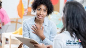A woman gestures with her hand on her chest while speaking to another person holding a clipboard in a classroom, reflecting how teachers advise parents about iep rights. The image includes the logo "a day in our shoes.