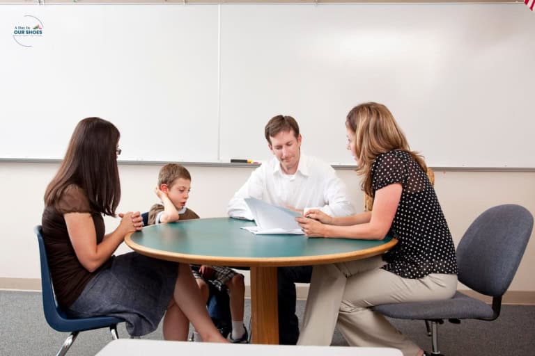 Parent seated at a table with educators during a school meeting, reviewing paperwork and discussing a student’s support needs.