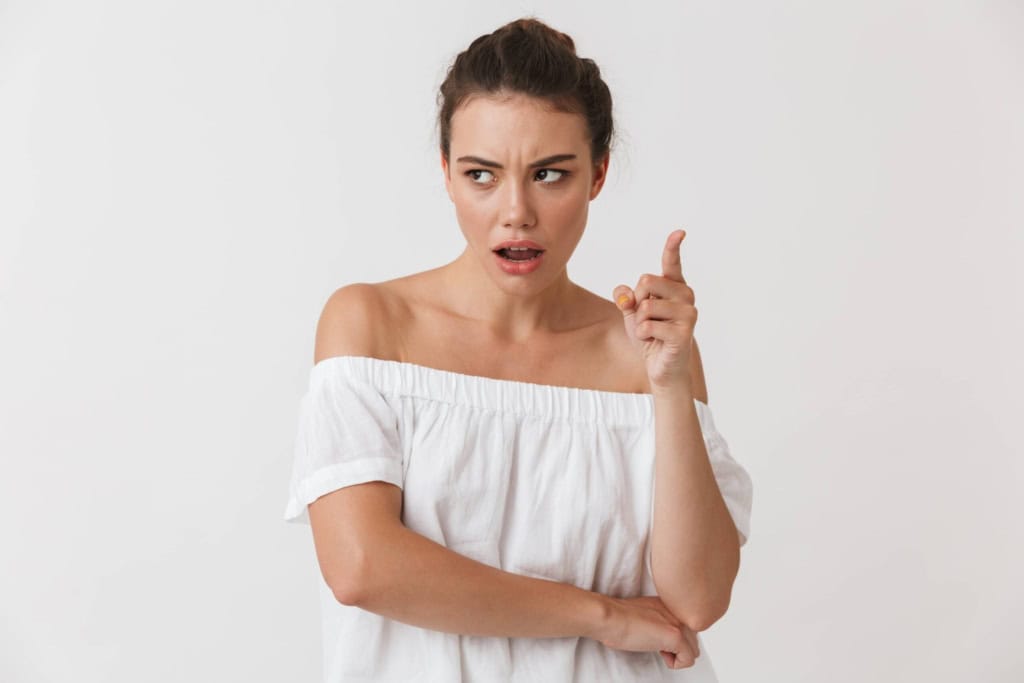 Woman with confused expression, pointing upward, wearing a white off-shoulder top.