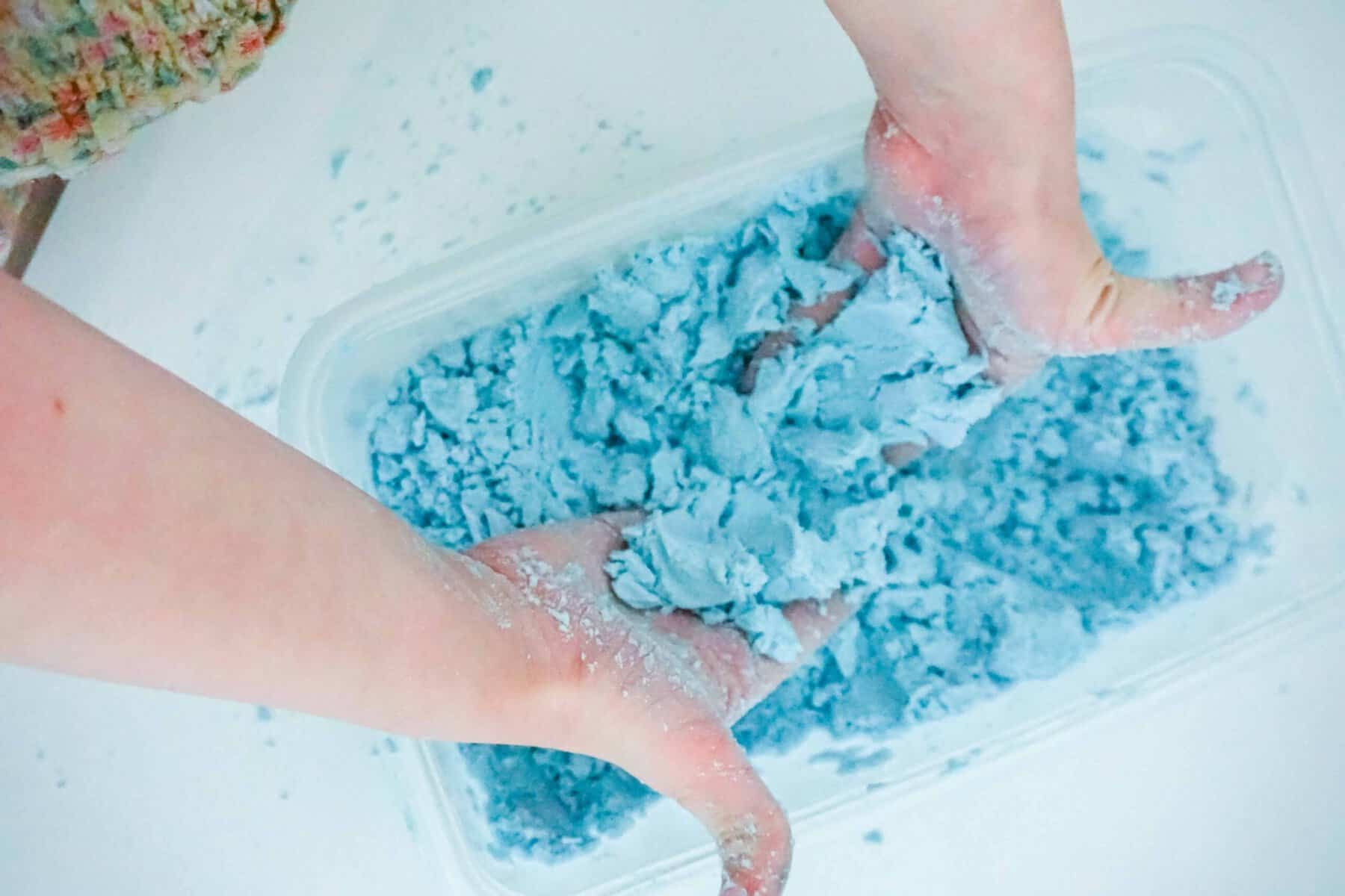 Child playing with blue kinetic sand in a clear container.