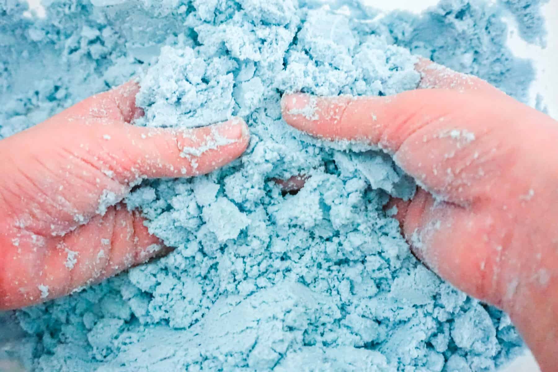 Child's hands playing with blue kinetic sand for sensory activity.